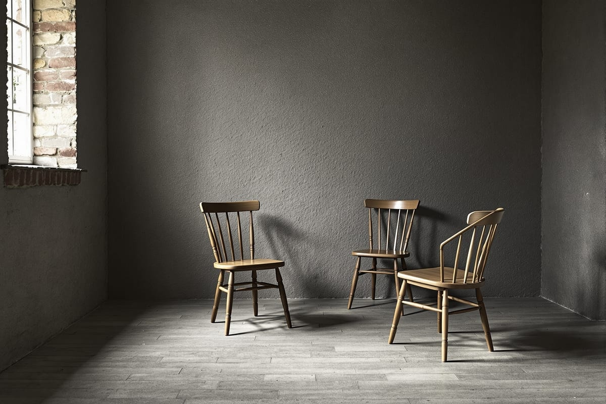 Two plain wooden chairs facing each other in an empty stone-walled room lit by a small window